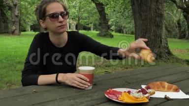 在橡树林的木桌上，穿着黑色手工衣服的漂亮女孩吃着美味的饭菜
